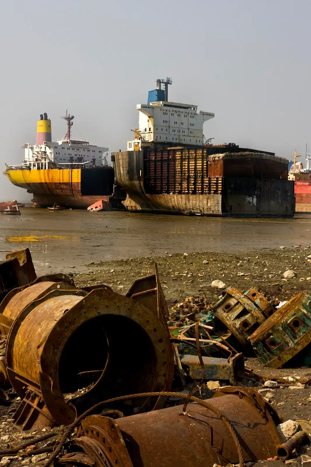 Ein Schiffswrack an der Küste von Chittagong, Bangladesh. Im Vordergrund sind verrosstete Überreste eines anderen Schiffs zu sehen, die an Land gespült wurden.