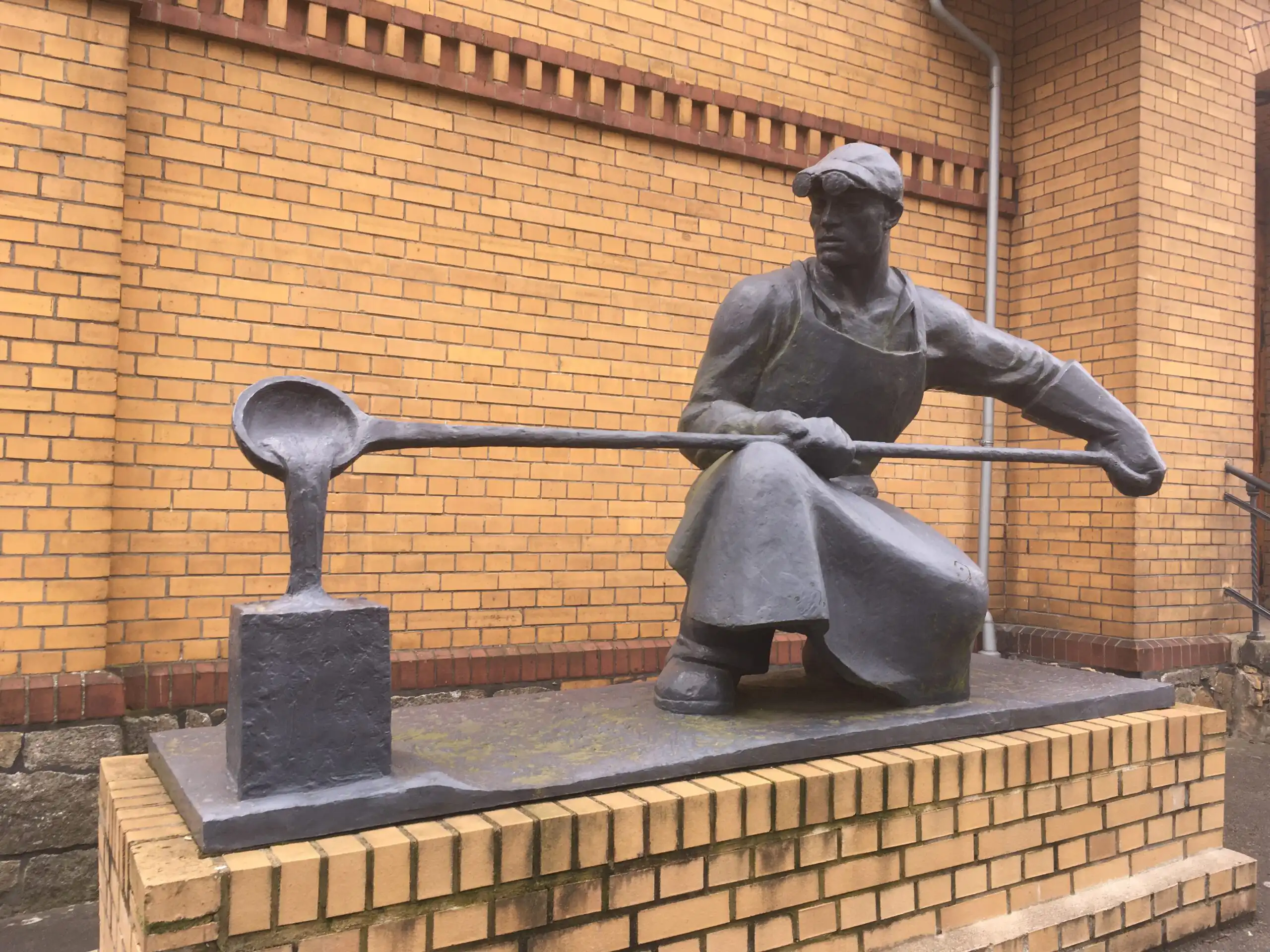 Statue eines Fabrikarbeiters, der aus flüssigem, heißen Metall eine Figur gießt (Kunstguss)