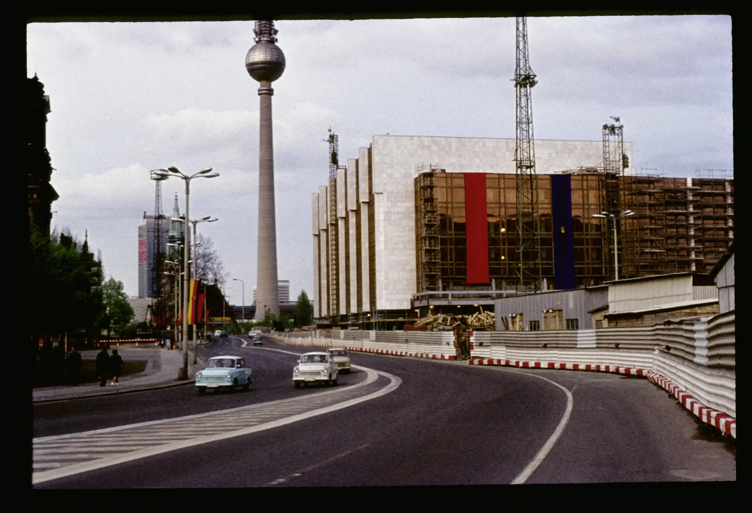 Stadtmitte von Ost-Berlin mit Blick auf den Fernsehturm und den Palast der Republik. Auf der Straße fahren drei Trabis.