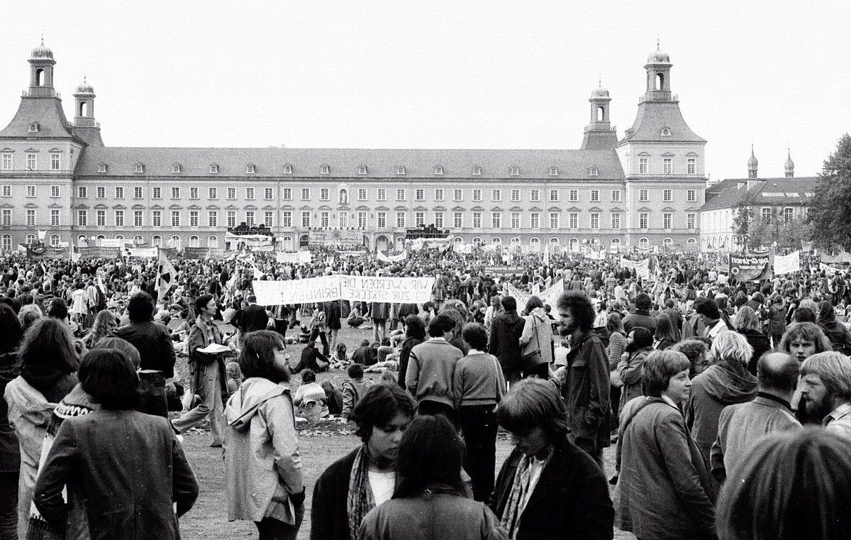 Anti-Atomkraft Demo in Bonn 1979: Tausende Menschen stehen auf der Hofgartenwiese vor dem Hauptgebäude der Uni Bonn. Einige halten Schilder und Banner in die Luft.