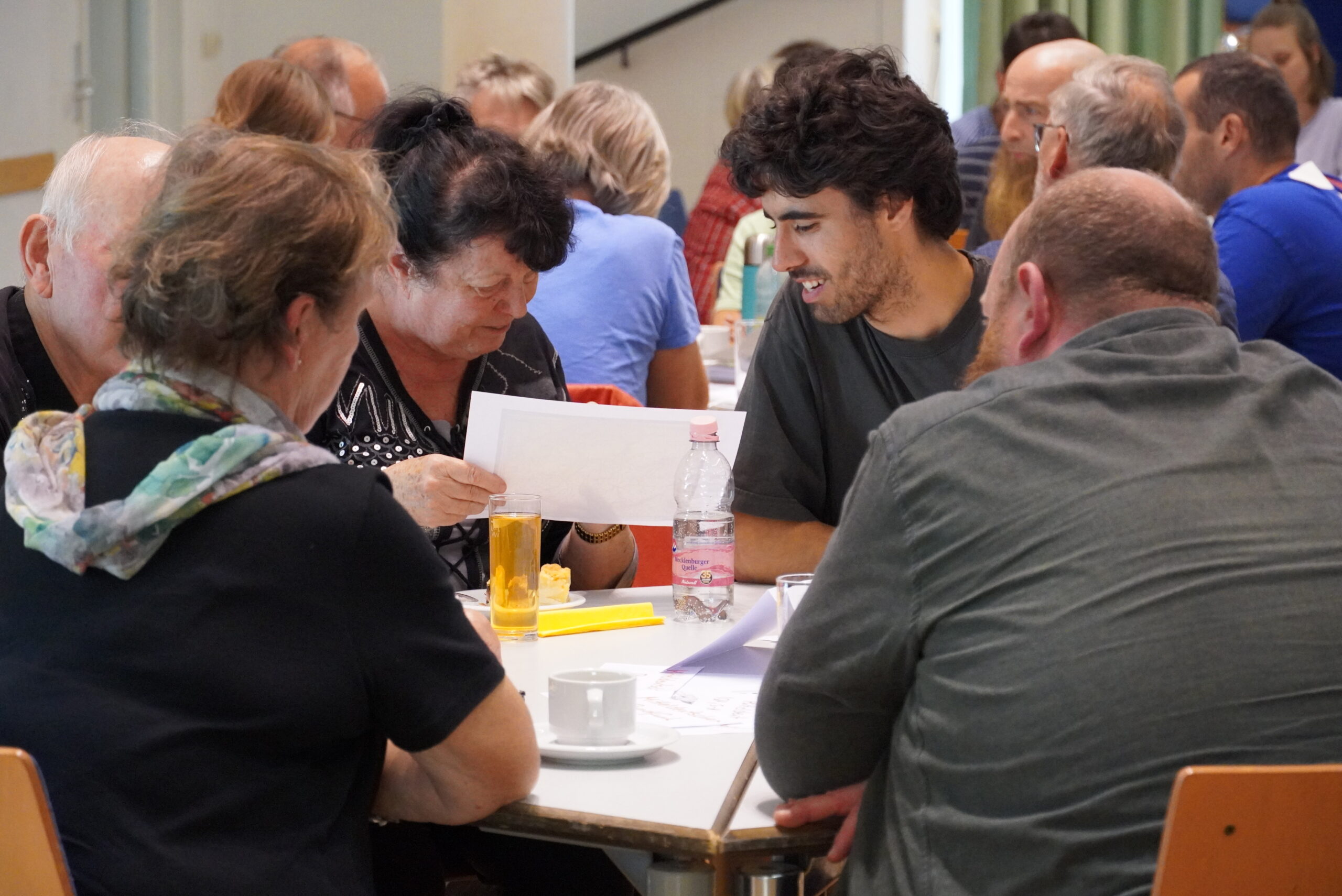Teilnehmende des Moving Labs in Borna sitzen gemeinsam am Tisch, diskutieren und betrachten Fotos.