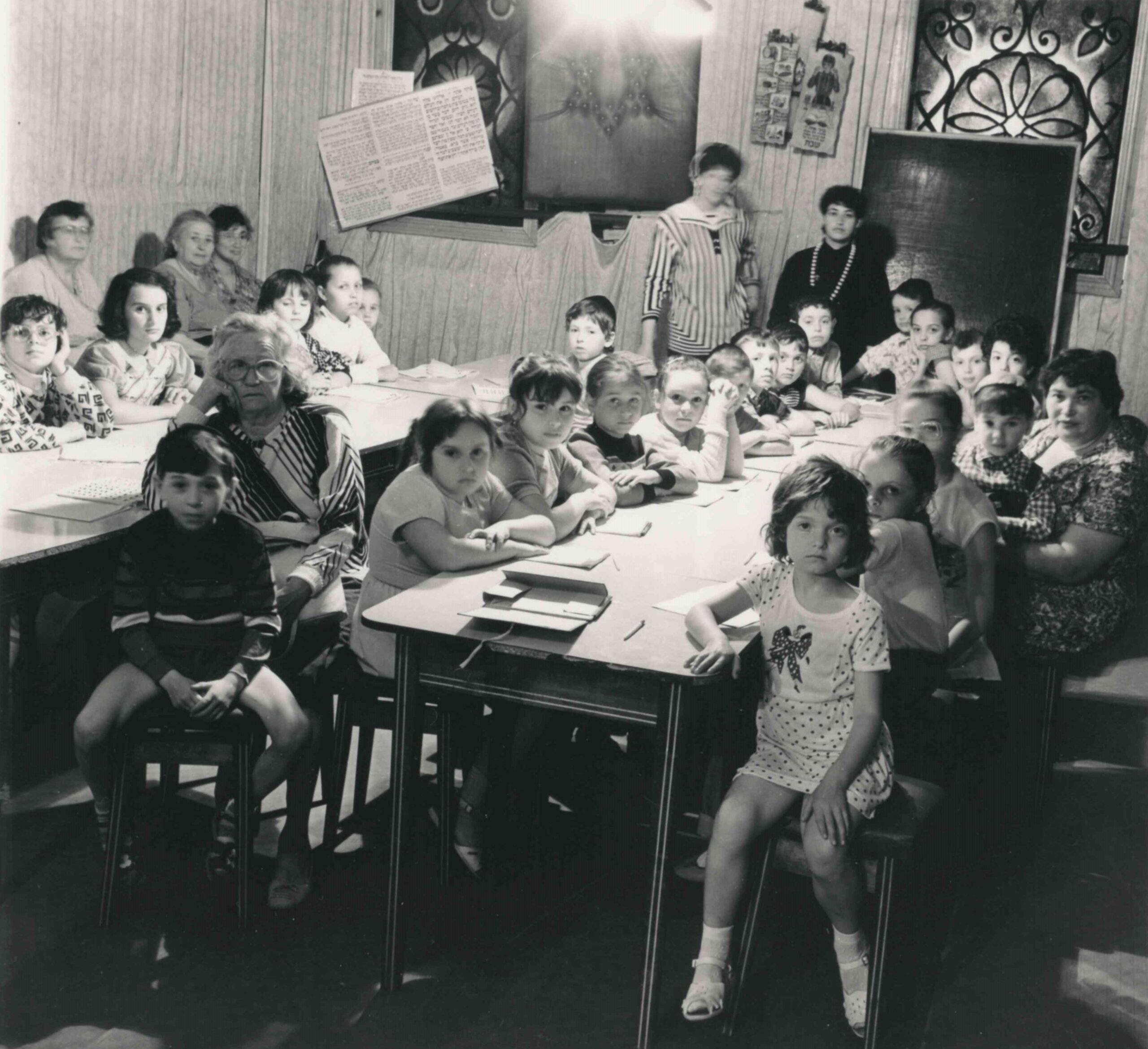 Kinder sitzen mit ihrer Lehrerin gemeinsam an einem langen Tisch