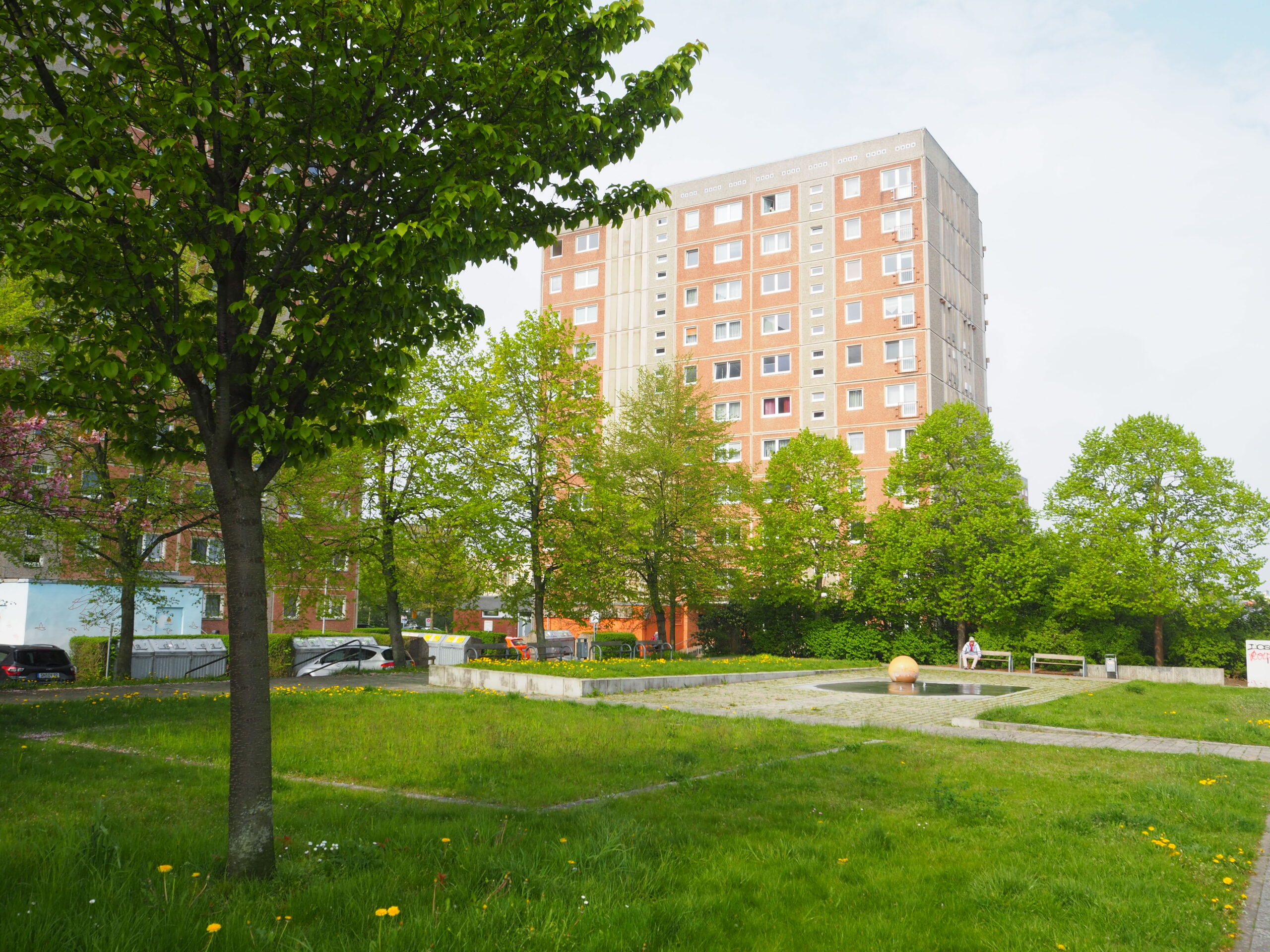 Eine Gr&uuml;nfl&auml;che mit B&auml;umen, dahinter ein Plattenbau.