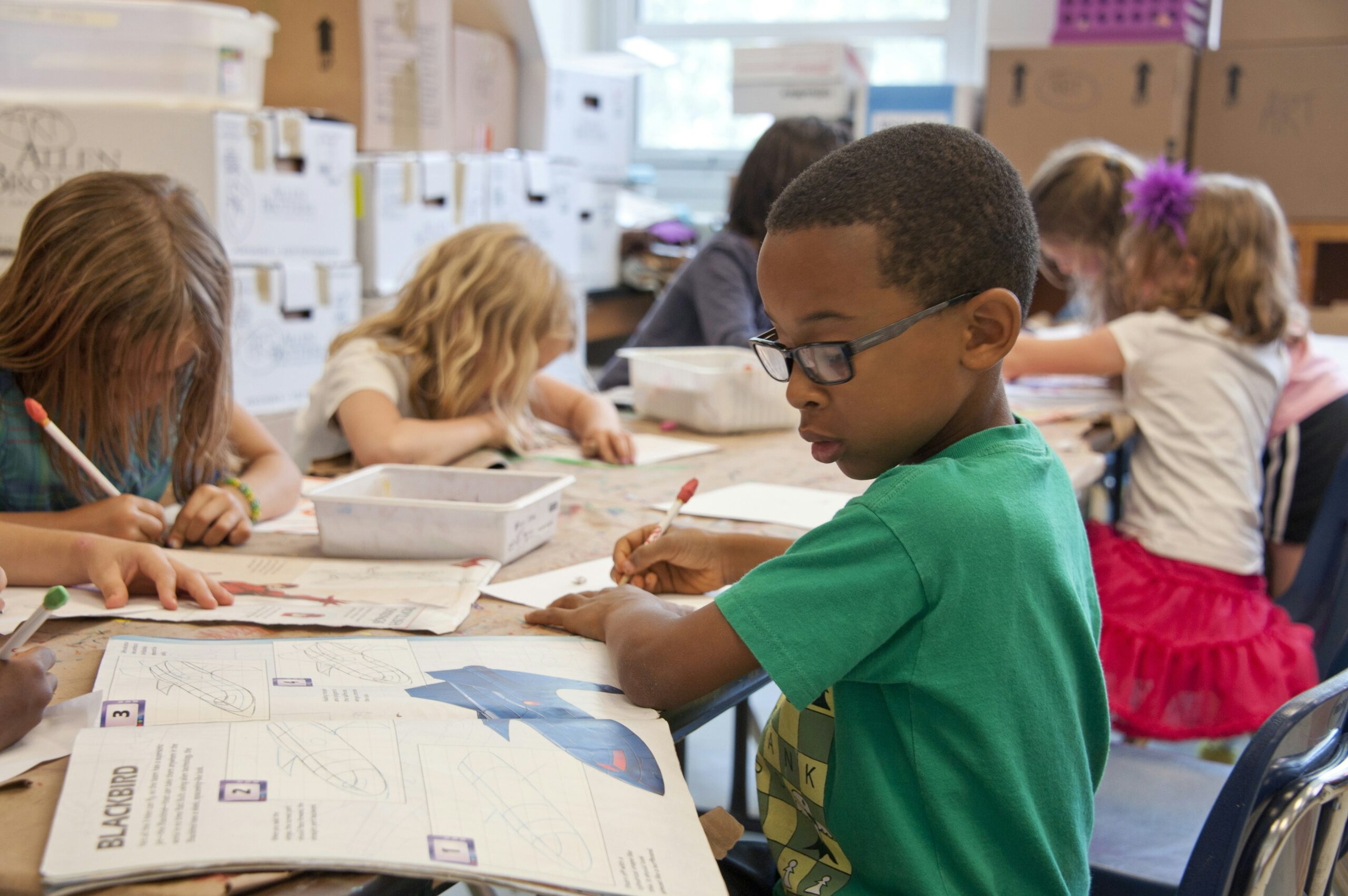 Kinder sitzen am Tisch und erledigen Schulaufgaben mit ihren Schulb&uuml;chern