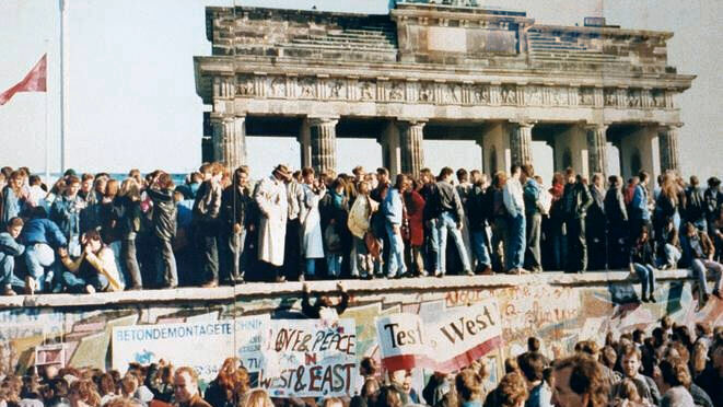 Menschen stehen auf der Berliner Mauer vor dem Brandenburger Tor