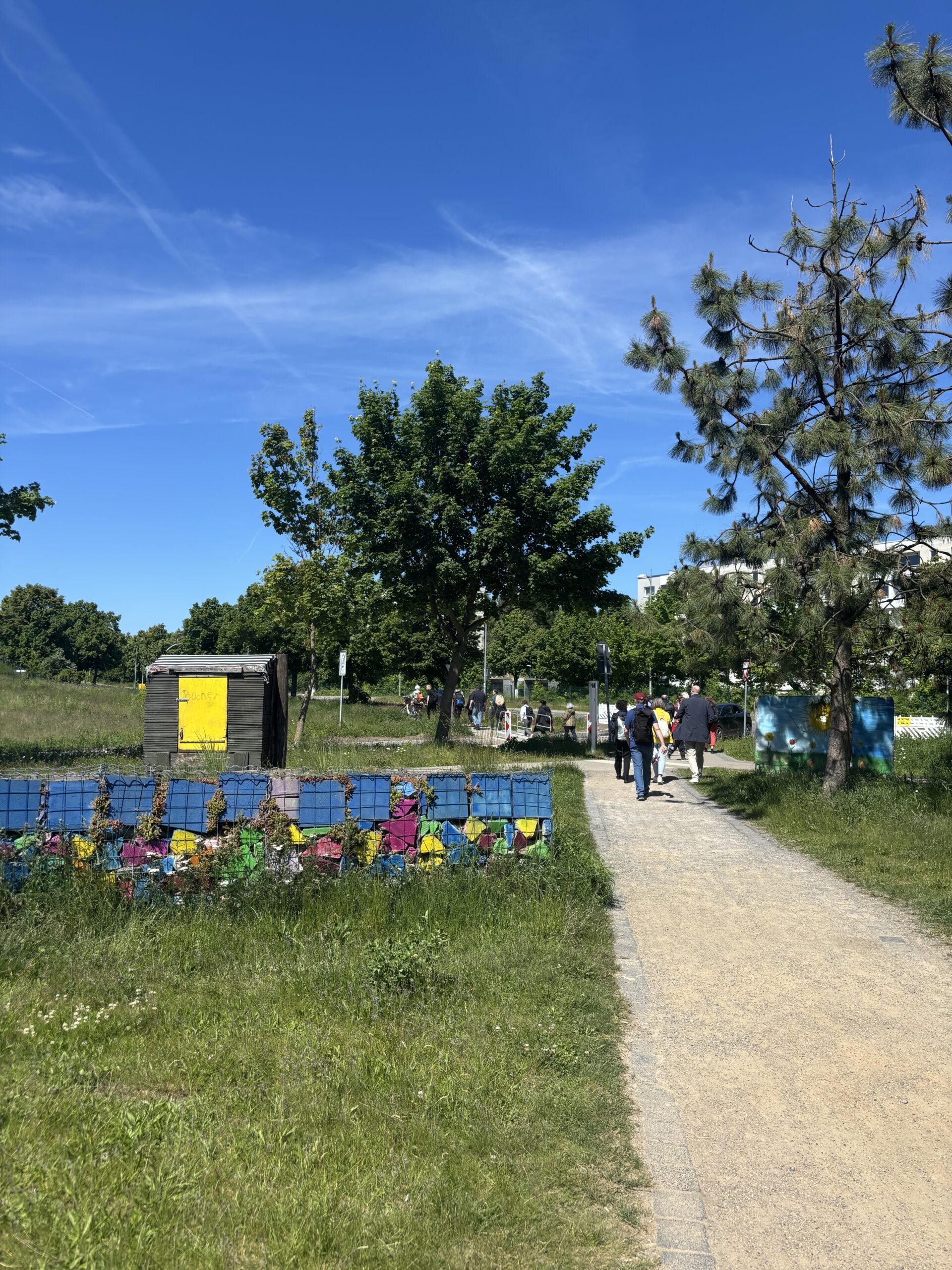 Der Plattenpark: niedrige, bunt bemalte Mauerst&uuml;cke aus ehemaligen Plattenbauten stehen auf einer Wiese. Auf dem Weg daneben l&auml;uft die Gruppe des Stadtspaziergangs.