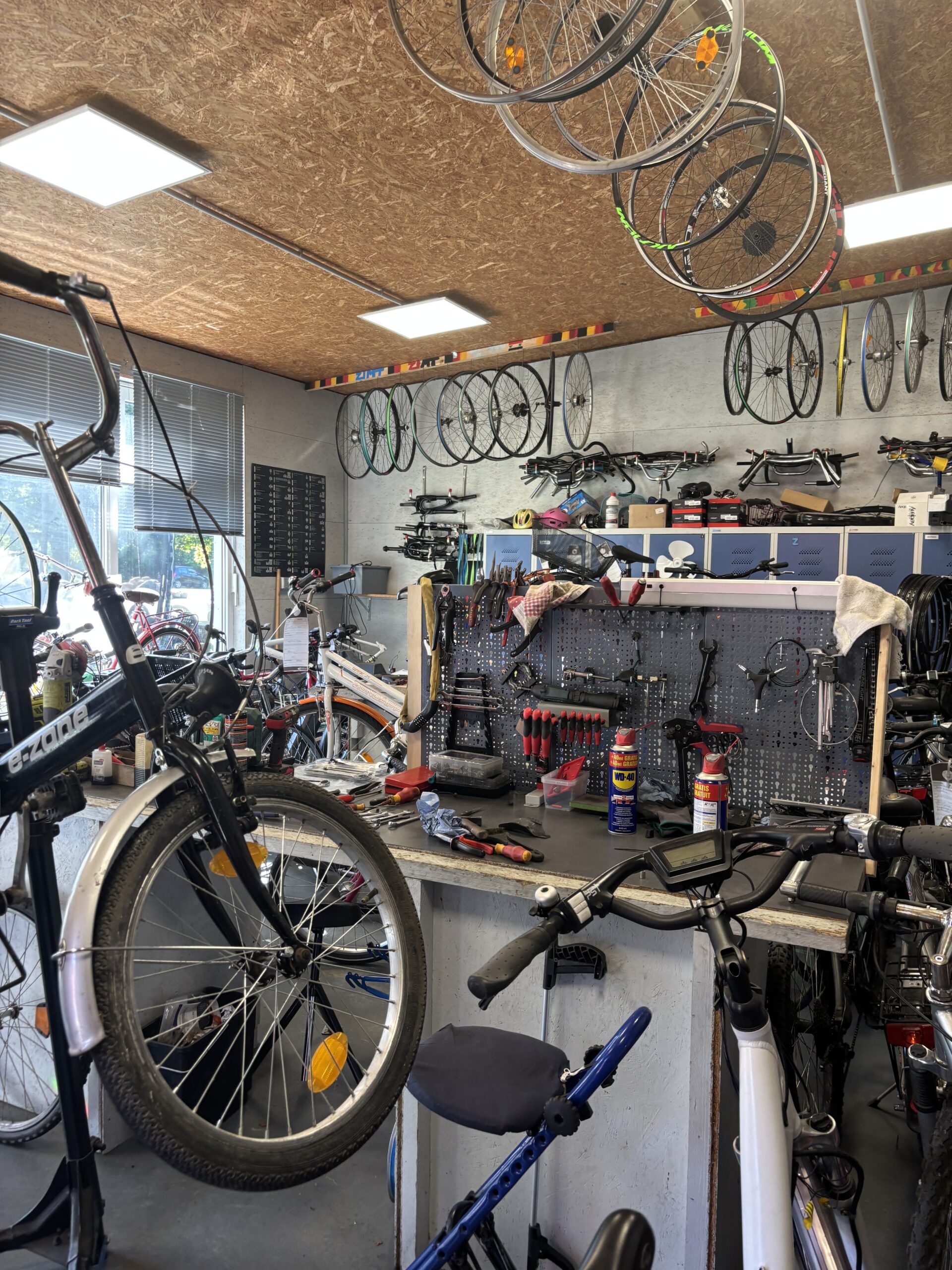Die Fahrradwerkstatt des ZiMT: Auf einer Werkbank liegt viel Werkzeug. Von der Decke h&auml;ngen dutzende R&auml;der.