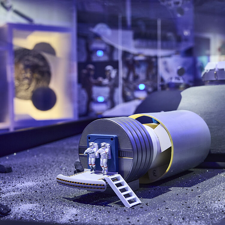 Ein Model von zwei kleinen Astronauten, die über einer Startplattform schweben, wahrscheinlich von einer Rakete.
